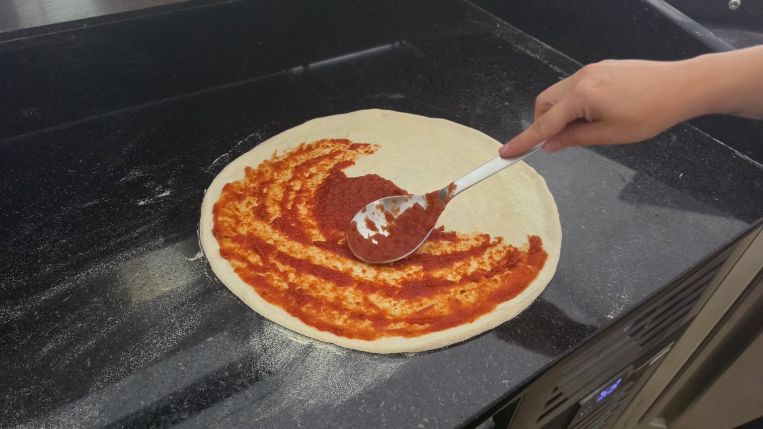 Tomatensauce wird von Hand auf einer FINISH PIZZA verteilt